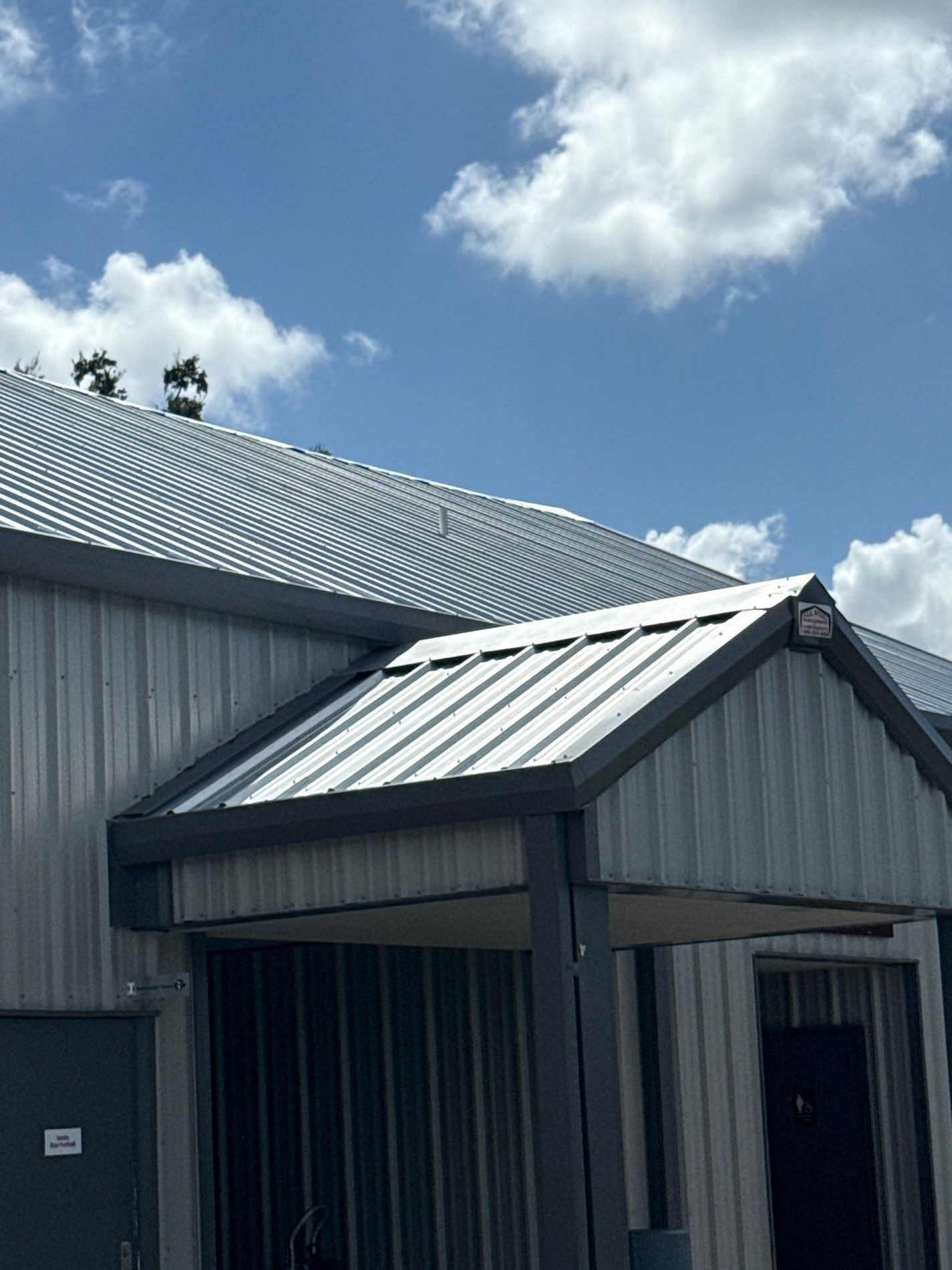 A silver corrugated metal building with a dark gray trim, under a blue sky with fluffy clouds.