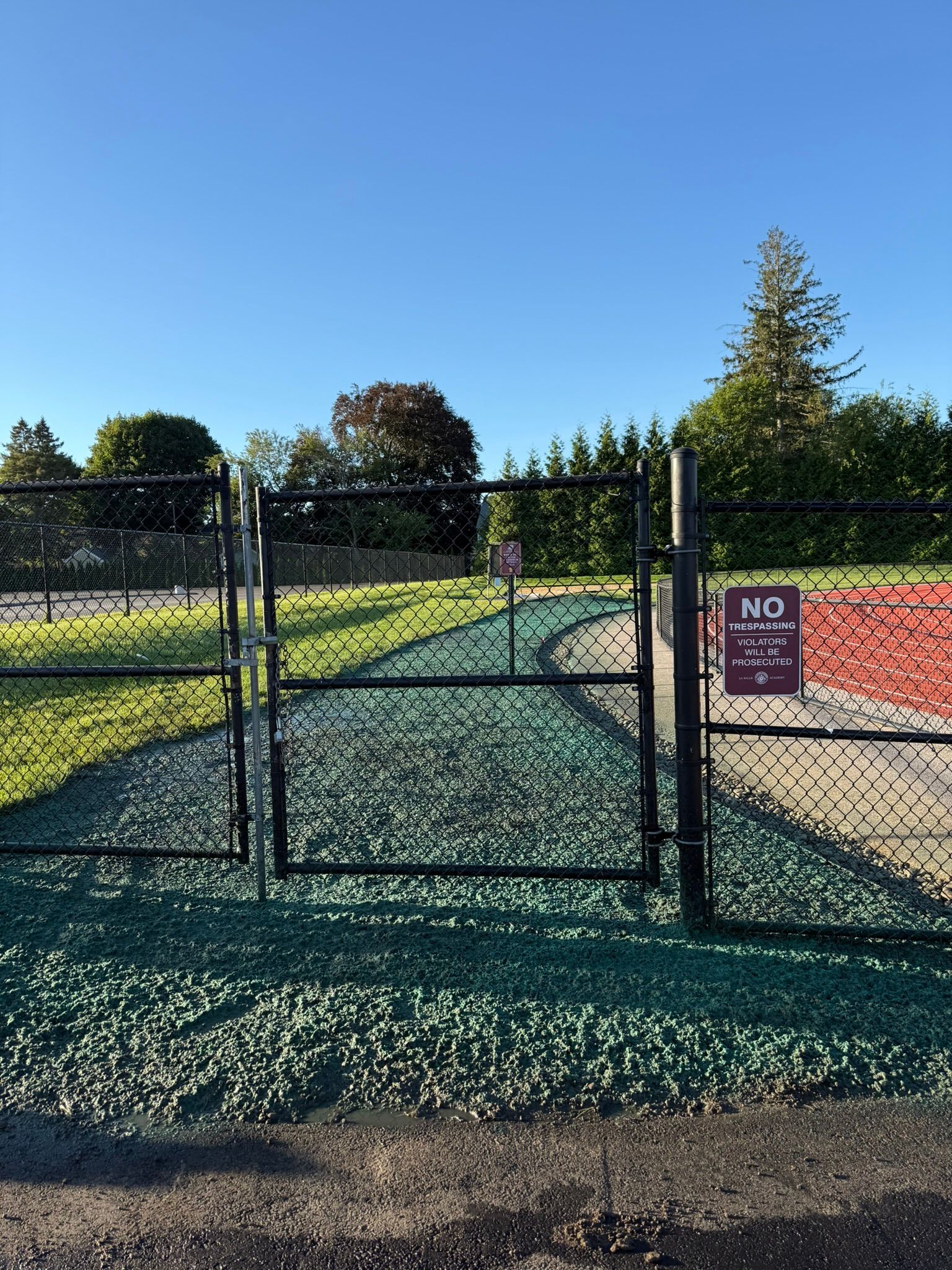 Black gate open to a green and red pathway in a park, with a 