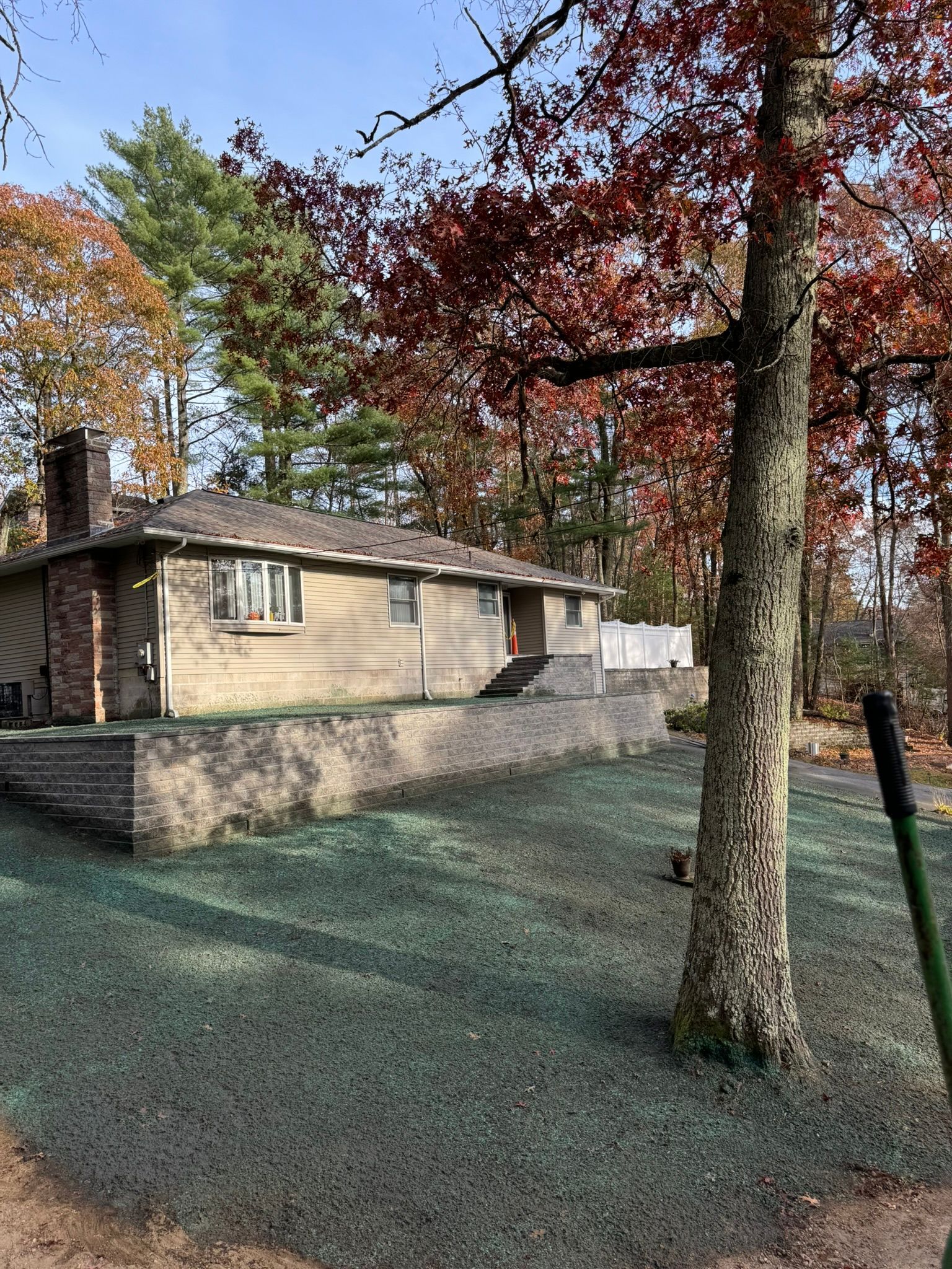 House with a brick chimney and retaining wall, surrounded by trees with fall foliage and newly seeded lawn.