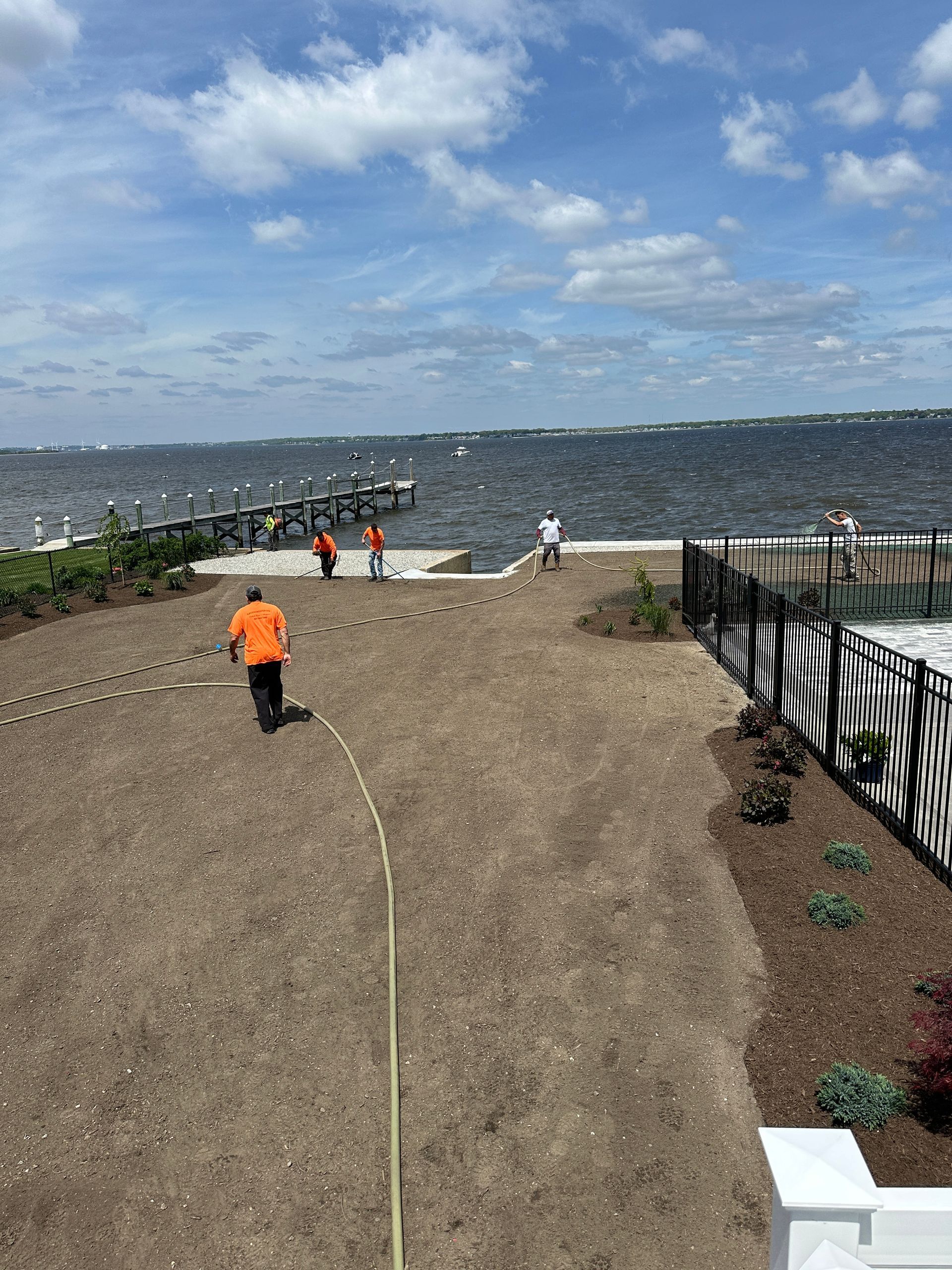 A man in an orange shirt is walking down a dirt path next to a body of water.