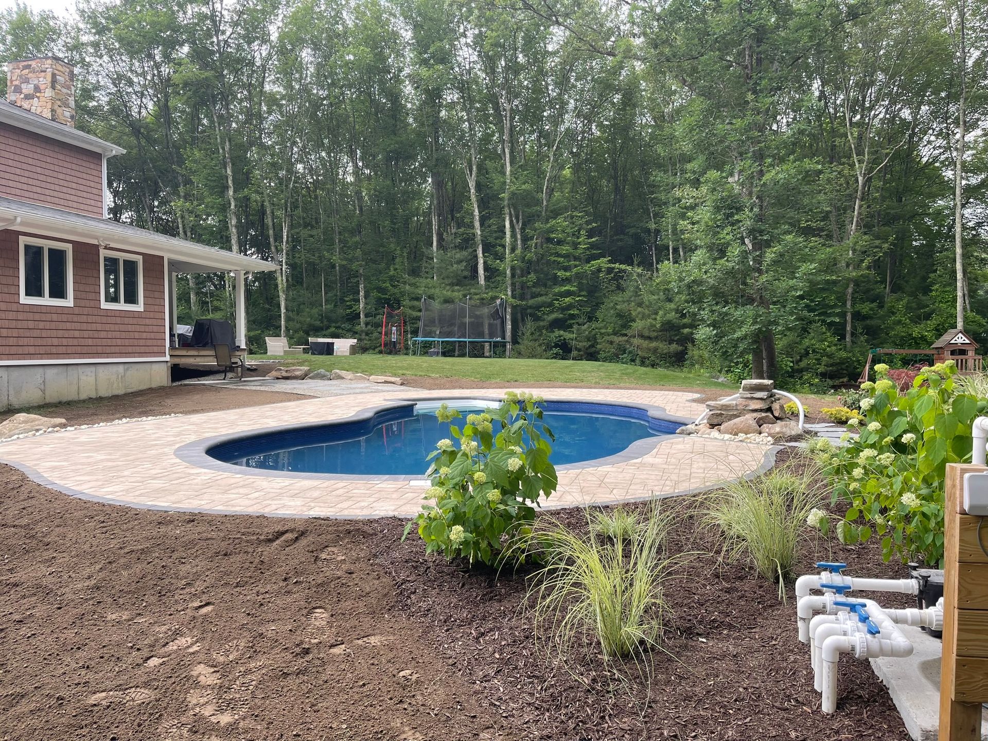 A large swimming pool is in the backyard of a house surrounded by trees.