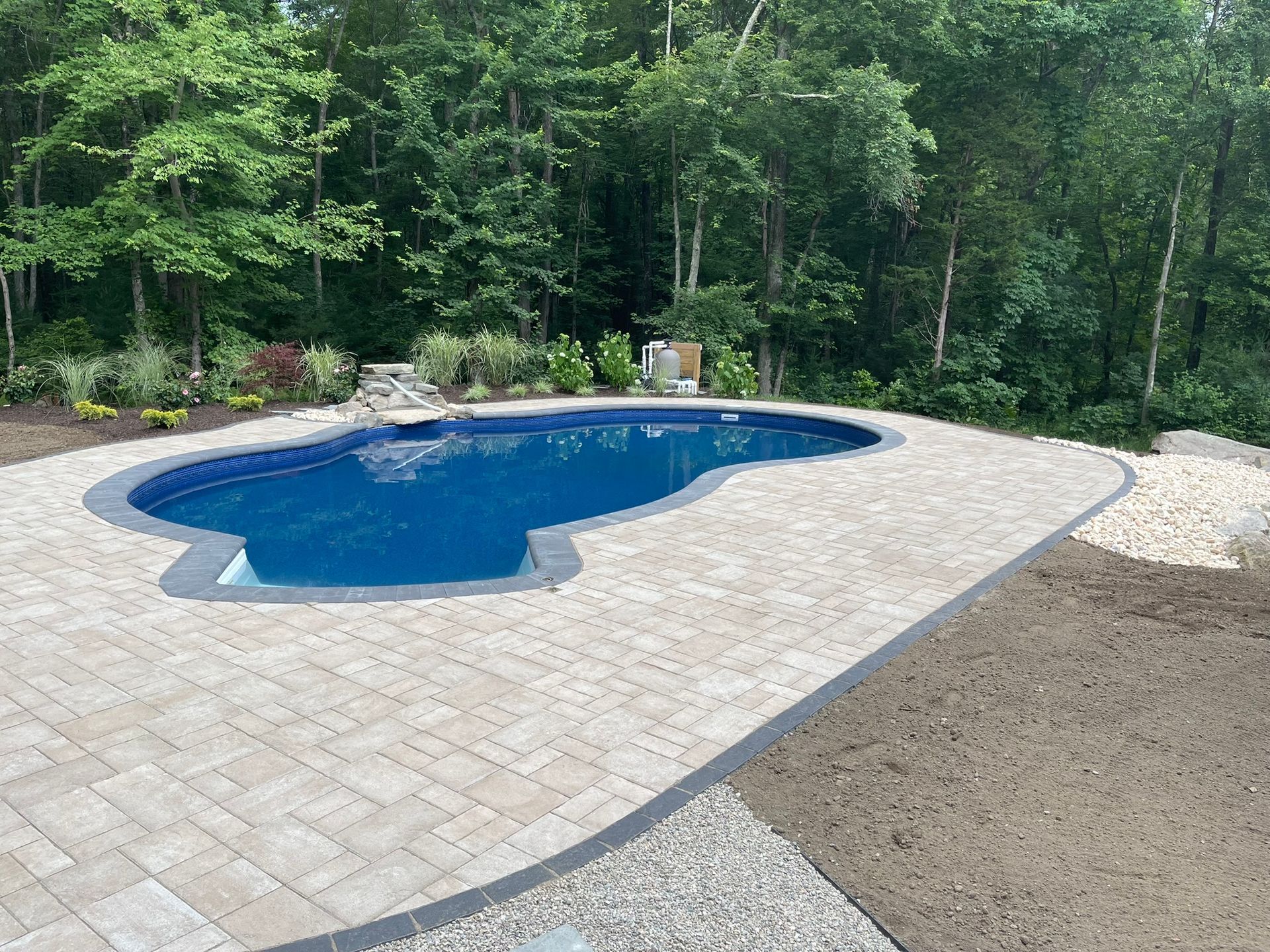 A large swimming pool is surrounded by a brick patio and trees.