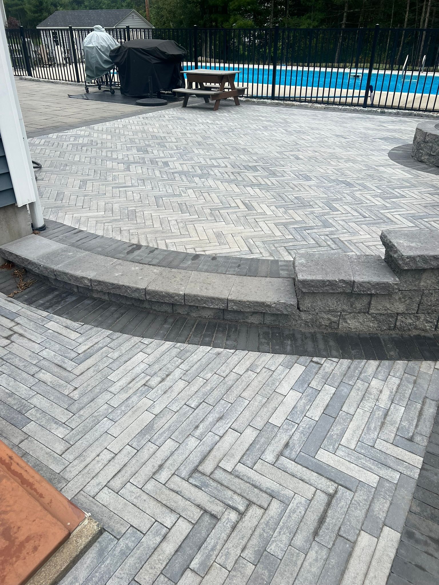 A patio with a herringbone pattern and a pool in the background.