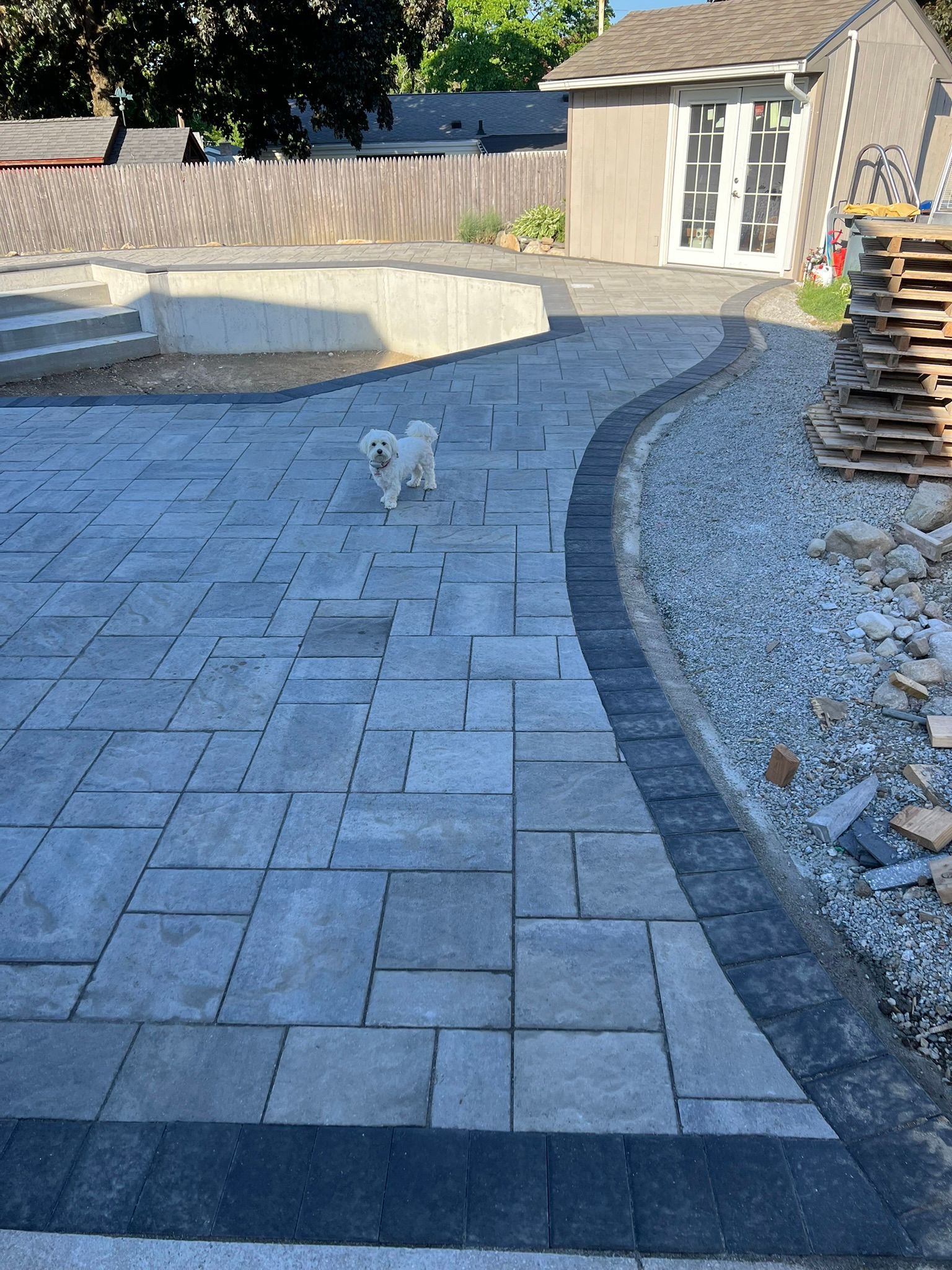 A small white dog is standing on a patio in front of a house.