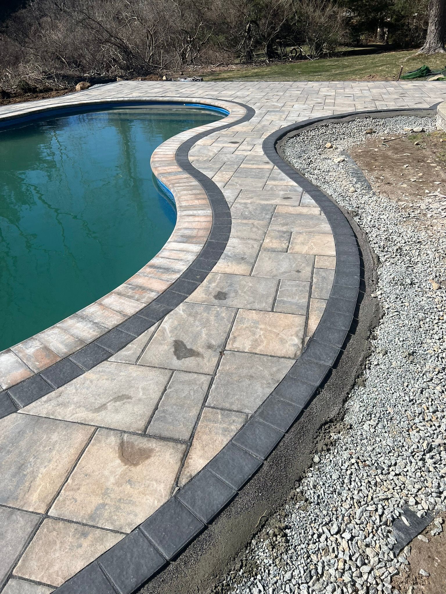 A swimming pool surrounded by a brick walkway and gravel.