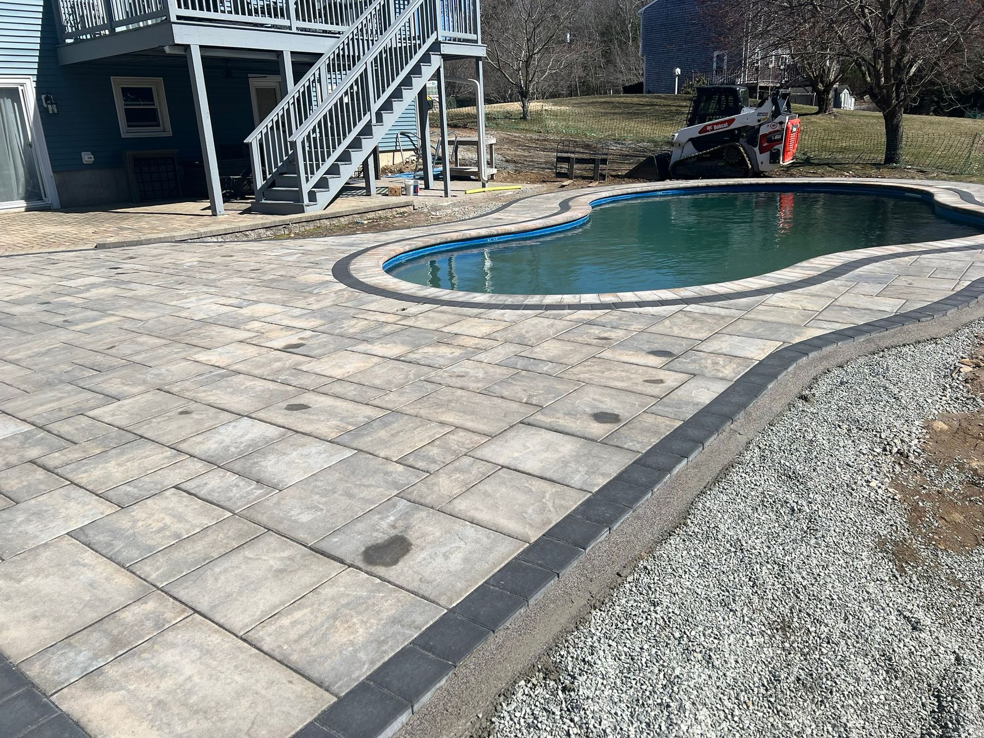 A large swimming pool is surrounded by a patio and gravel.