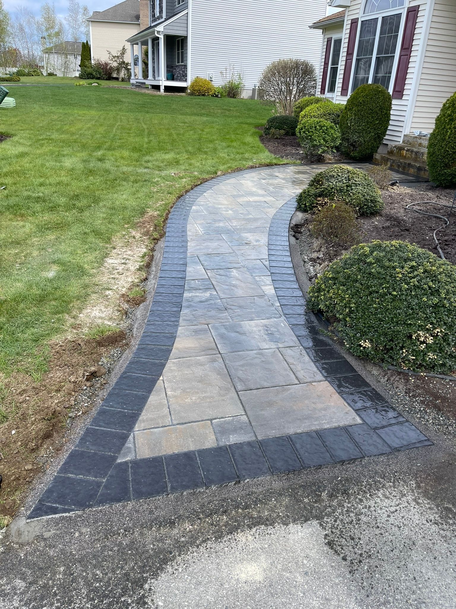 A brick walkway leading to a house with a lush green lawn.