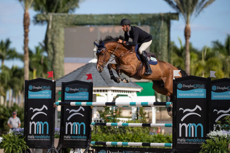 A man is riding a brown horse over a jump.