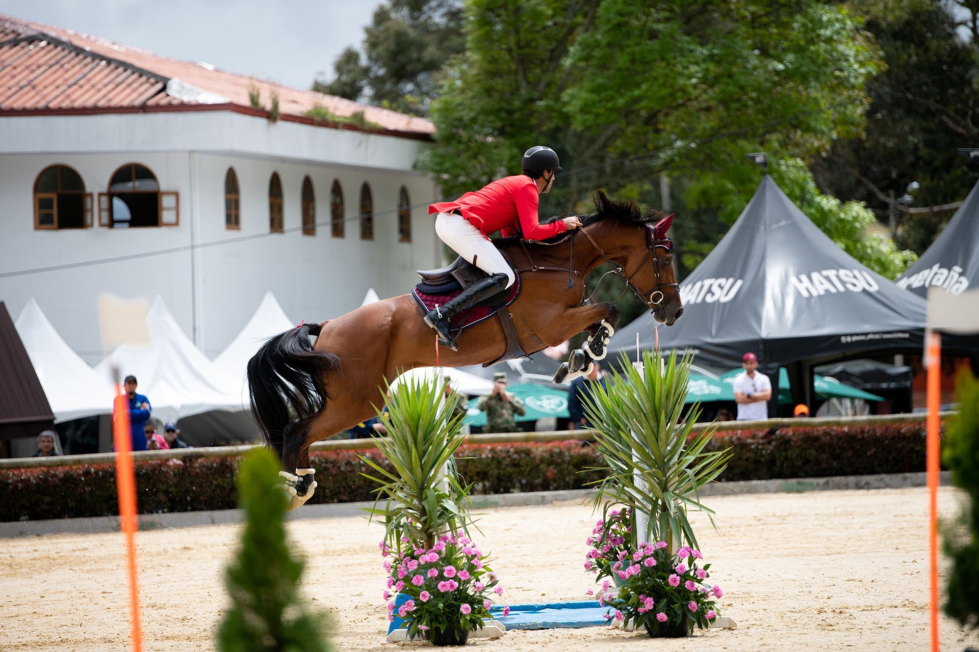 A man in a red jacket is riding a brown horse over a jump