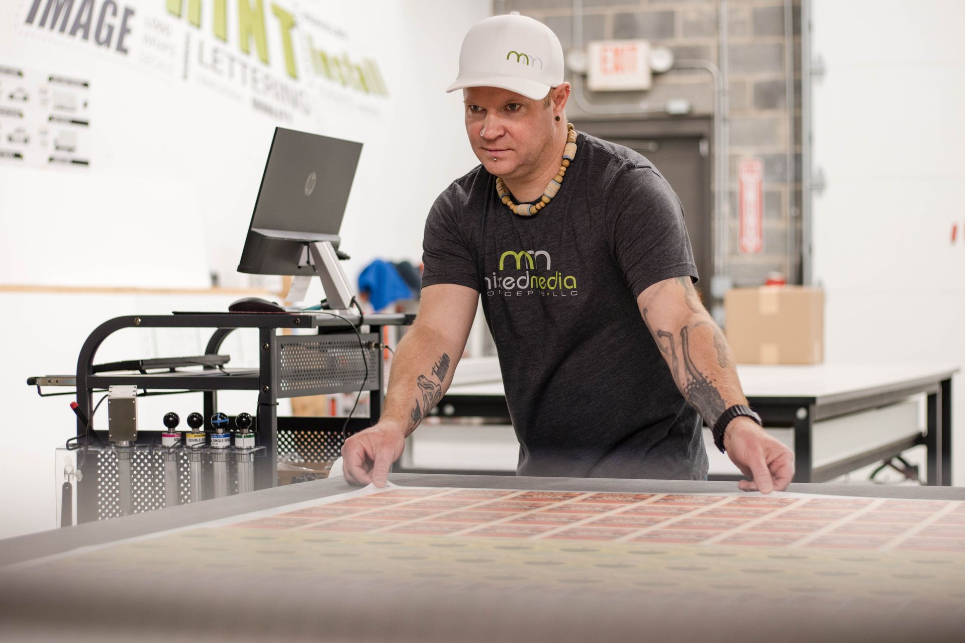 Man in a black shirt and white cap working at a large flatbed printer in a workshop
