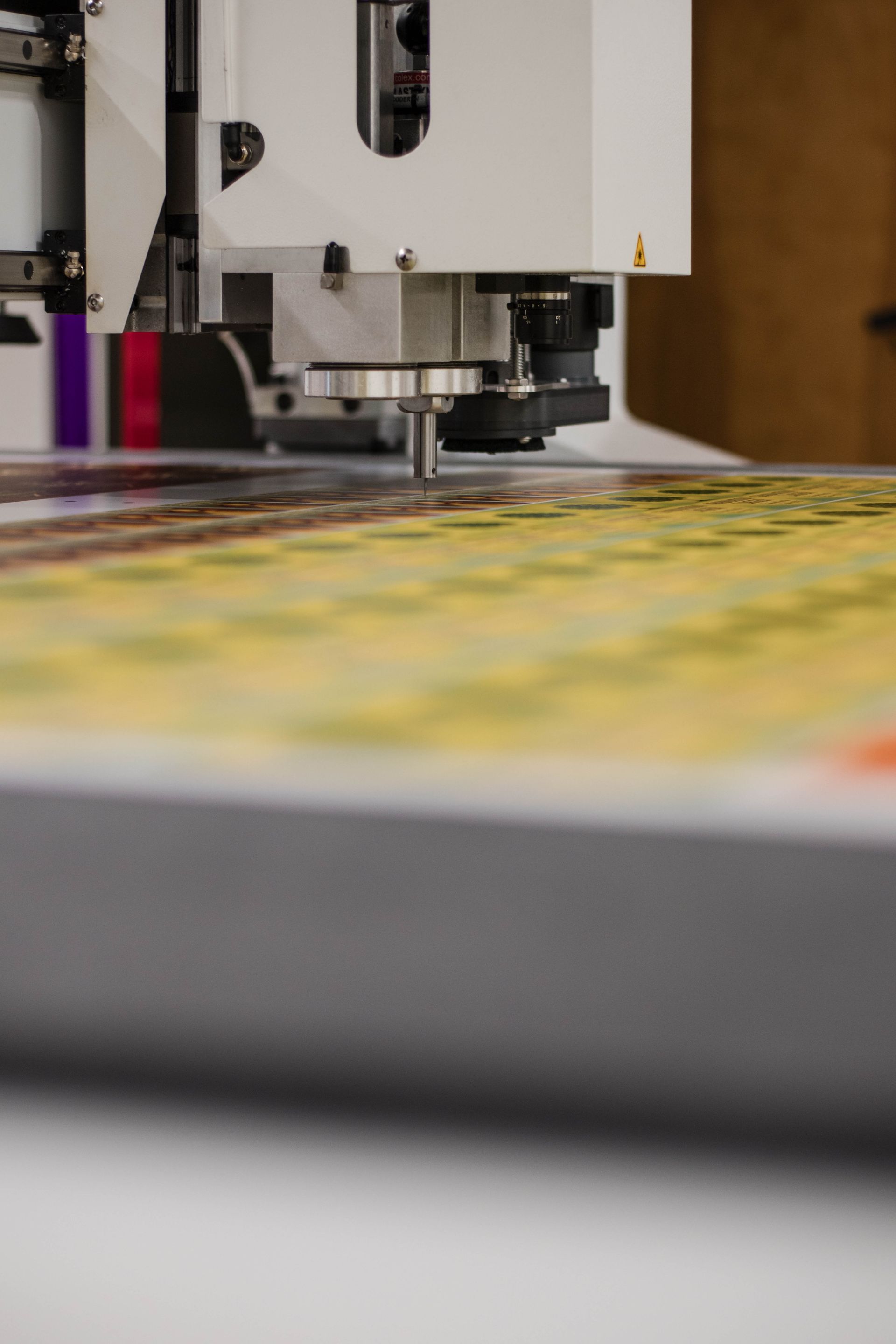 Close-up of a printing machine applying ink to a colorful sheet on a worktable