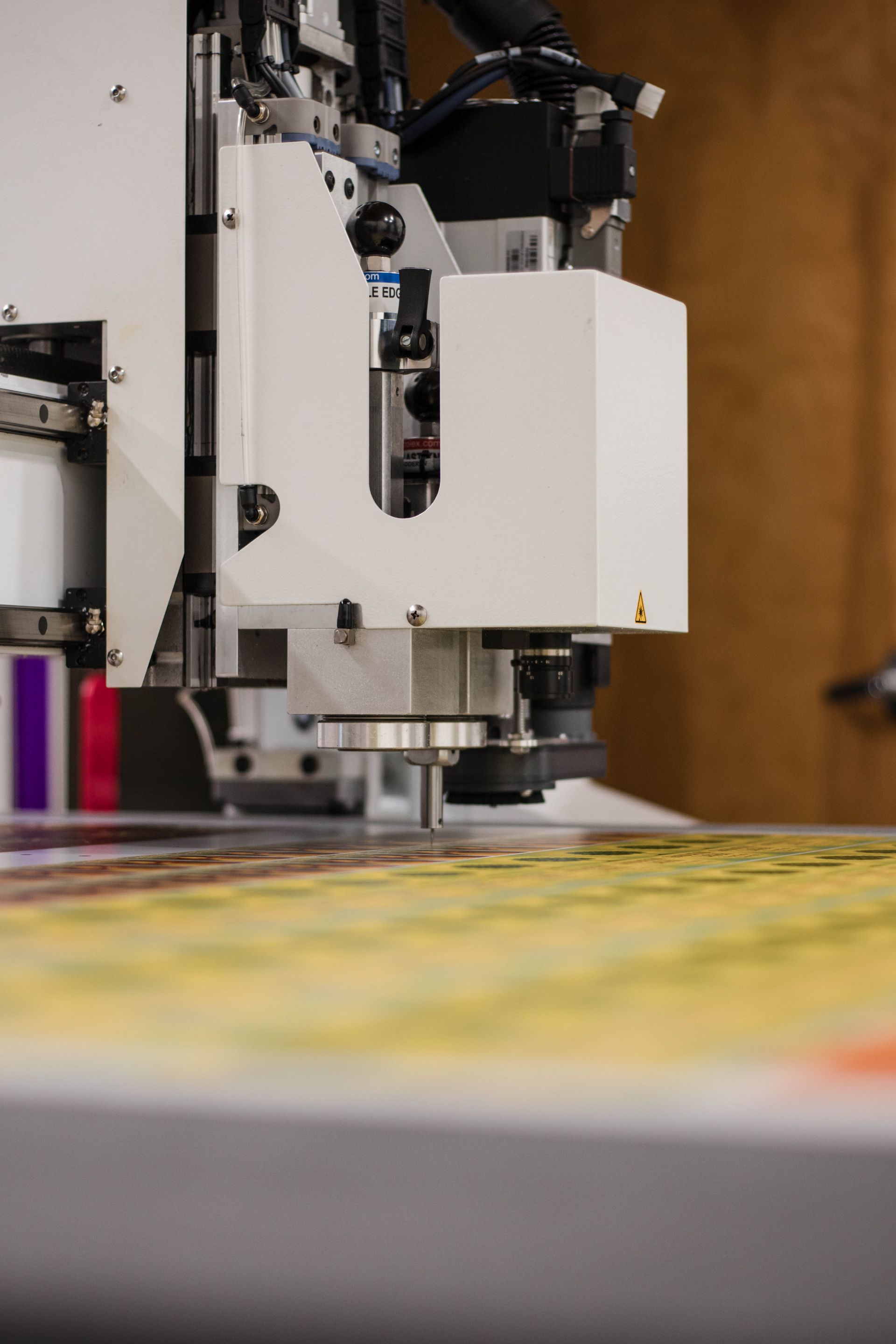 White industrial machine over a colorful printed surface in a workshop
