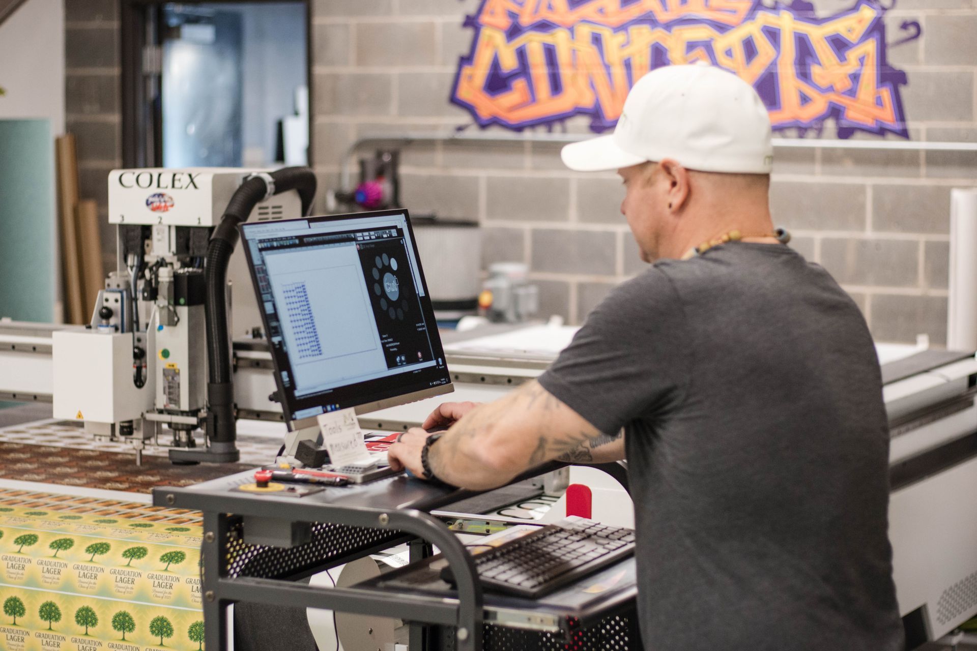 Person at a workstation using a computer in a print shop or workshop.