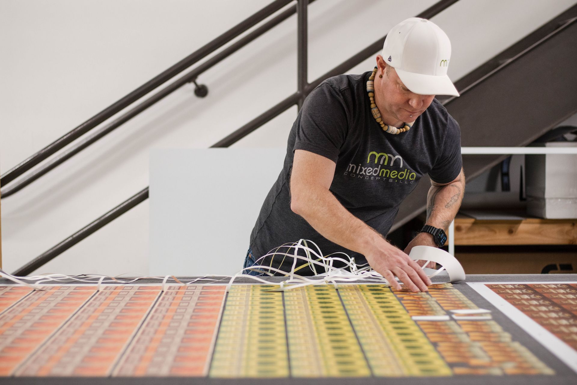 Worker in a white hard hat arranging cables on a colorful panel indoors