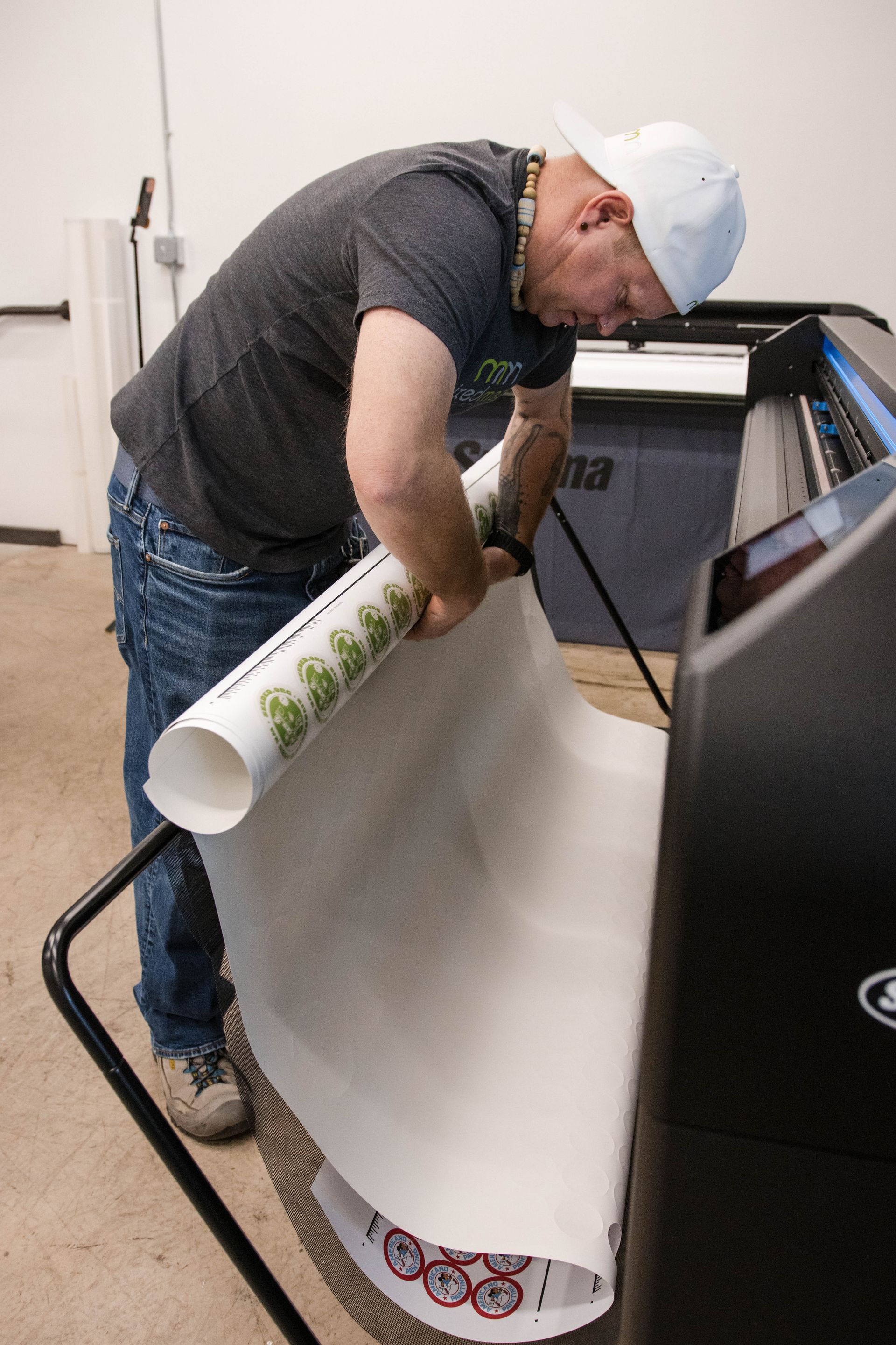 Man installing a large white banner onto a printer or plotter in a workshop