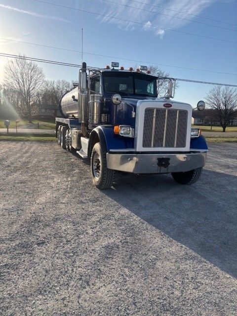 A blue peterbilt semi truck is parked in a gravel lot