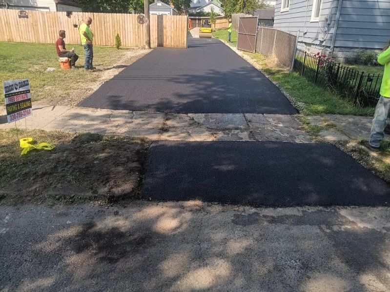 A group of men are working on a newly paved driveway.