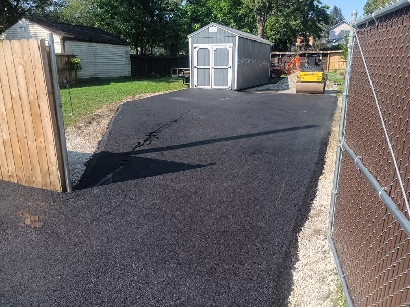 A shed is sitting in the middle of a driveway next to a chain link fence.