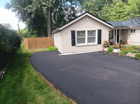 A small white house with a black driveway in front of it.
