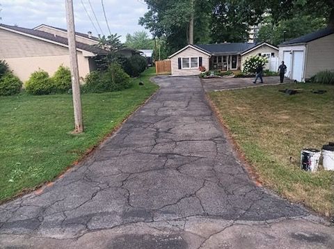 A cracked asphalt driveway leading to a house.
