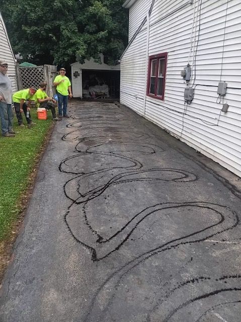 A group of people are working on a driveway in front of a house.