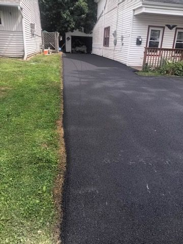 A black driveway leading to a house with a white house in the background.