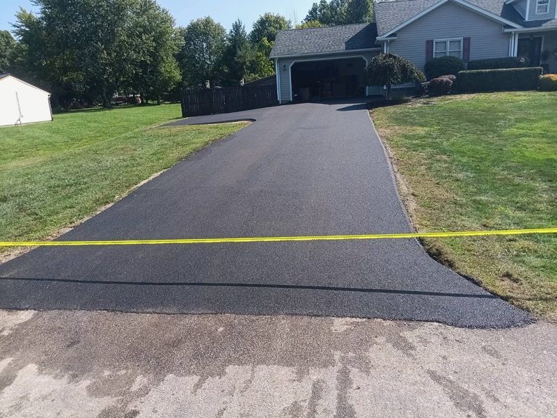 A driveway with a yellow tape along the side of it and a house in the background.