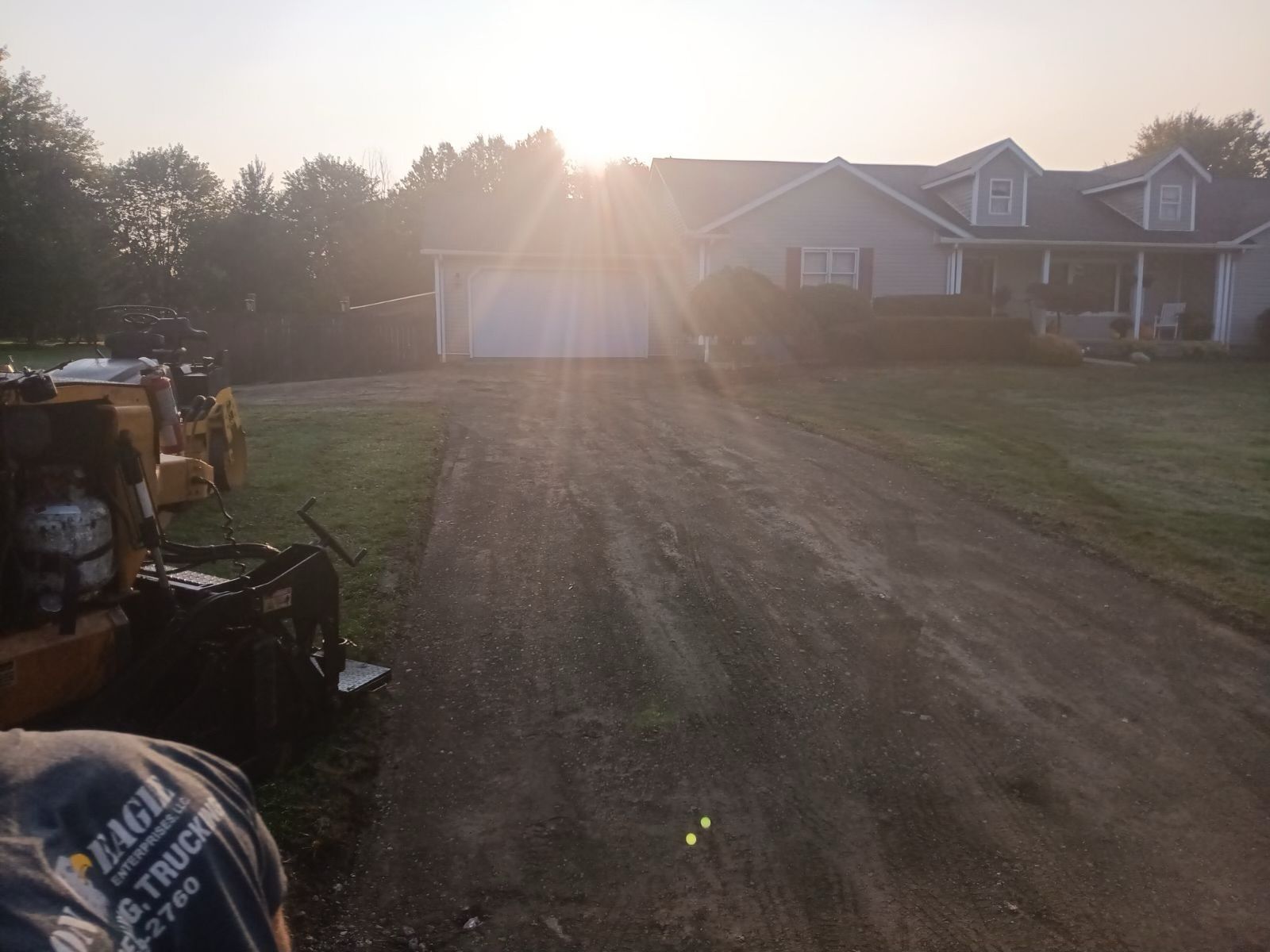 A dirt road leading to a house with the sun shining through the trees