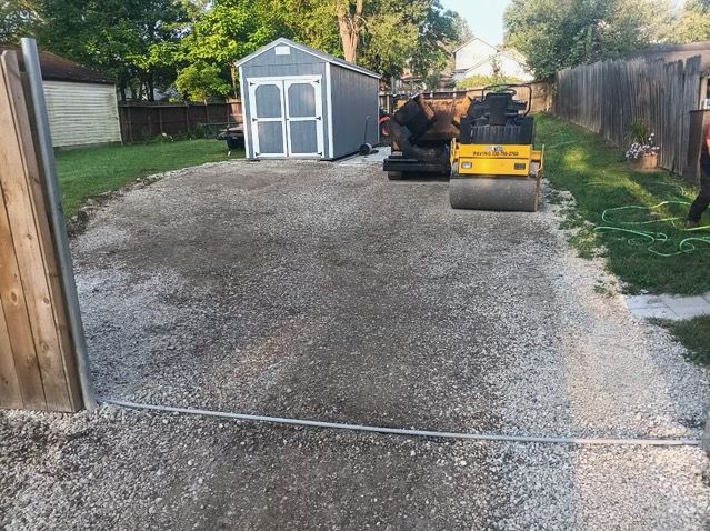 A gravel driveway with a shed in the background and a roller in the foreground.