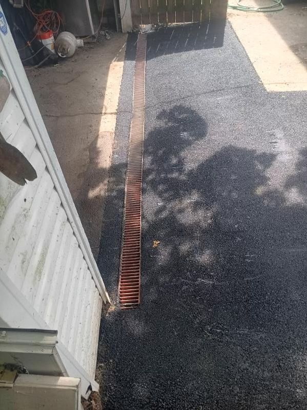 A drain on the side of a driveway next to a house.