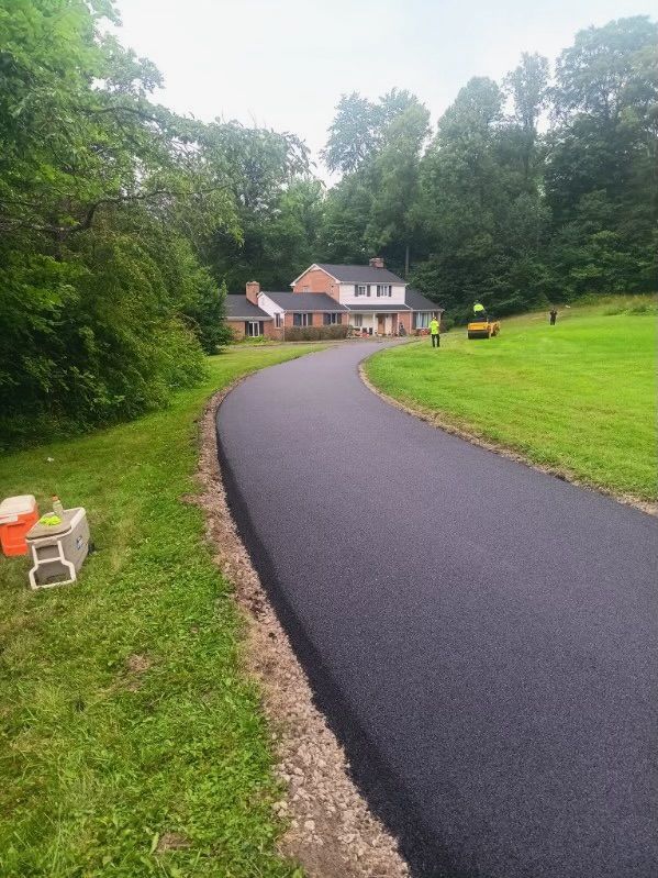 A newly paved driveway leading to a house in the middle of a lush green field.