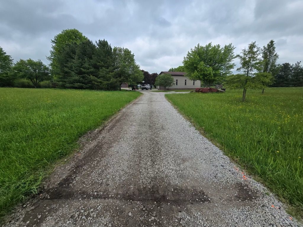 A dirt road leading to a house in the middle of a grassy field.
