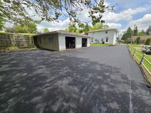 A black asphalt driveway with a white house in the background.