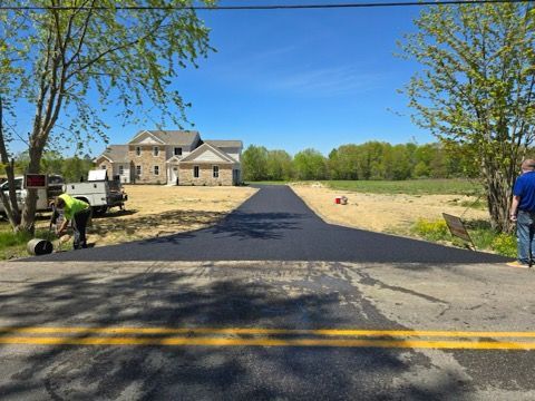 A man is laying asphalt on the side of a road.