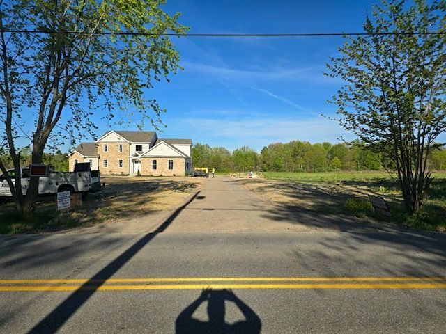 A shadow of a person is cast on the road in front of a house under construction