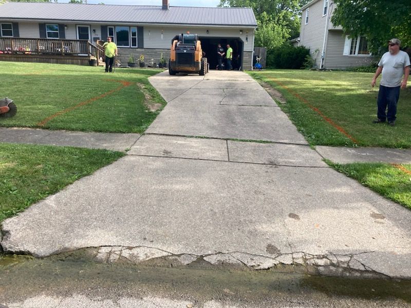 A group of people are working on a driveway in front of a house.