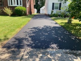 A driveway leading to a house with a brick house in the background.