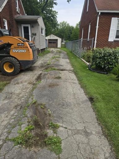 A skid steer is parked in a driveway next to a brick house.