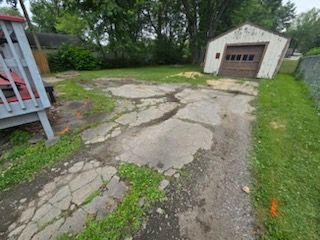 A cracked concrete driveway with a garage in the background.