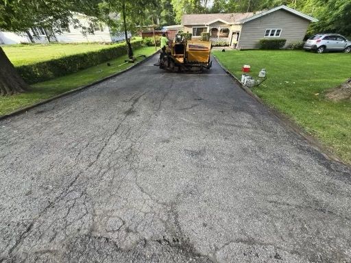 A machine is laying asphalt on a driveway in front of a house.