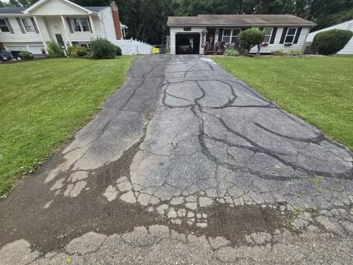 A cracked asphalt driveway leading to a house.