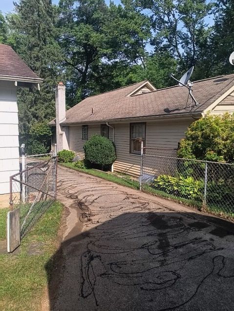 A house with a satellite dish on the roof is surrounded by trees and a chain link fence.