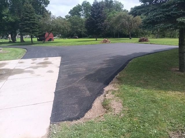 A newly paved driveway is surrounded by grass and trees.