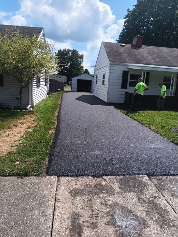 A man in a green shirt is standing on a driveway next to a house.