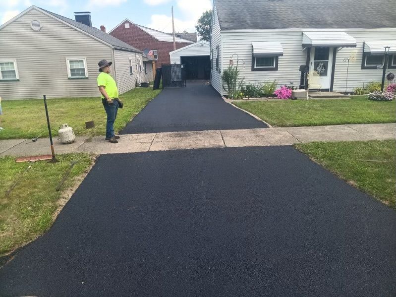 A man is standing in front of a house looking at a newly paved driveway.