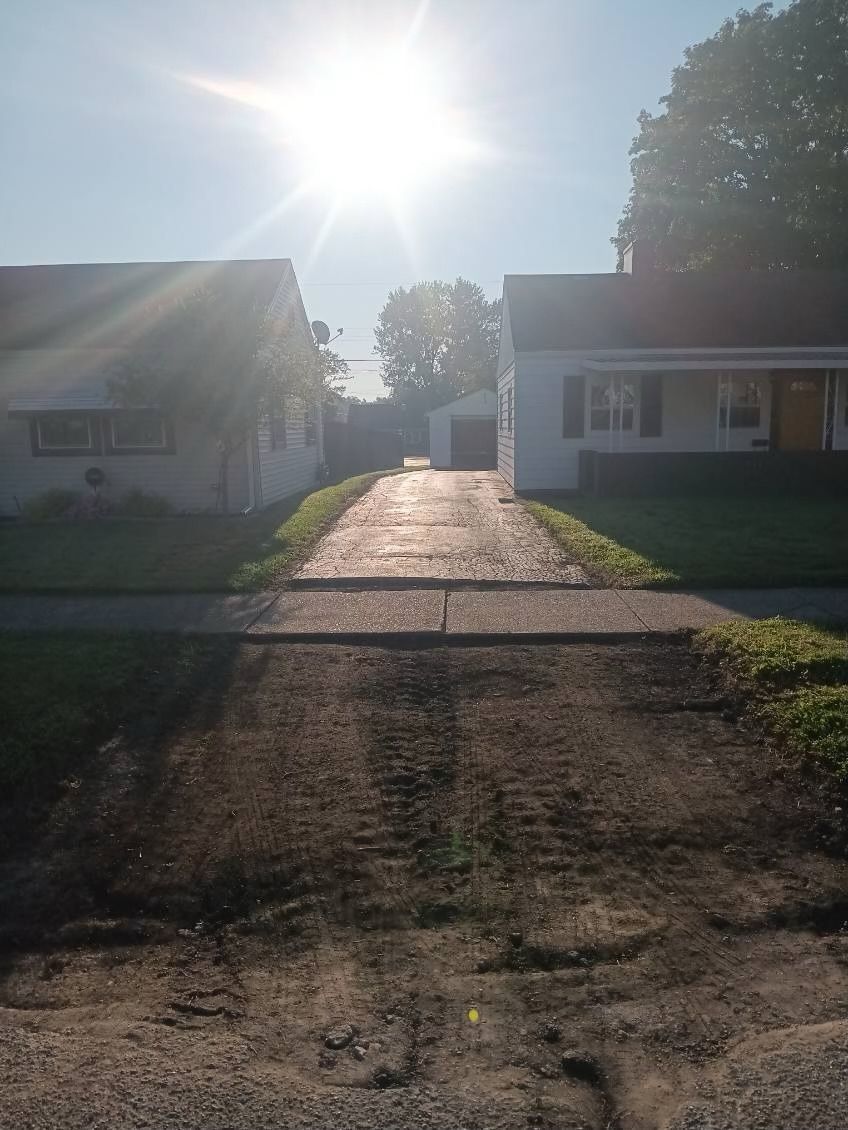 A driveway leading to two houses with the sun shining through the trees.