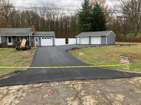 Newly paved asphalt driveway leading to a house and detached garage. Yellow caution tape is across the foreground.