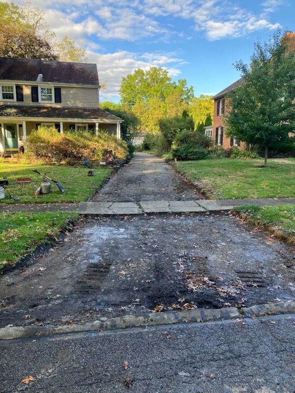 Asphalt driveway with stone border between houses, overcast sky.