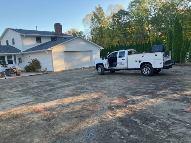 White work truck parked on gravel driveway next to a white house with a garage.