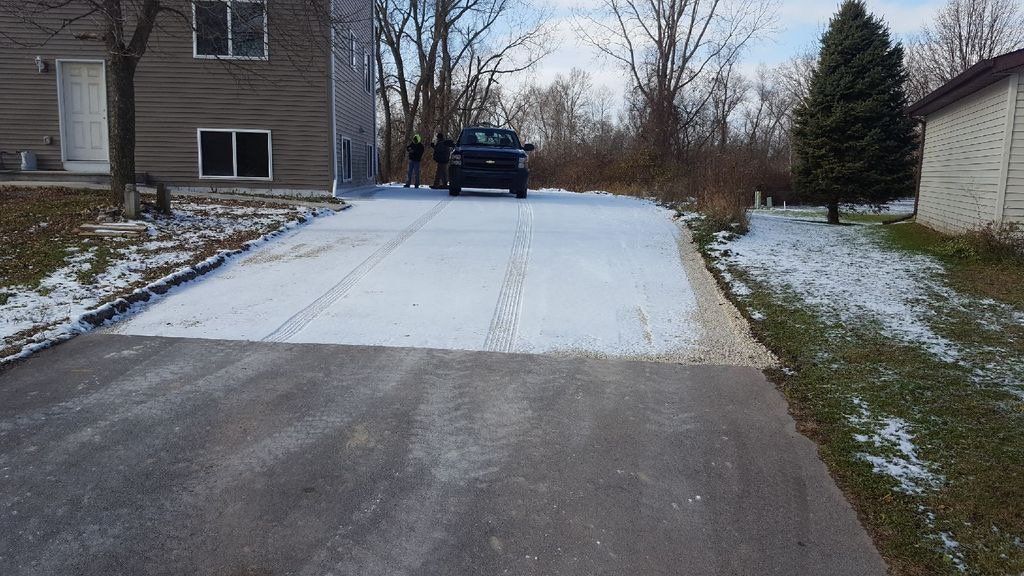 A car is parked on a snowy driveway next to a house.